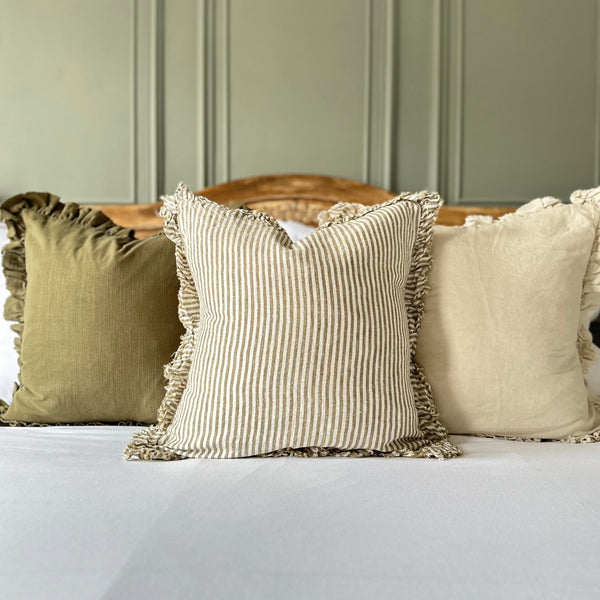 cream cushion with a ruffled edge and with a thick chunky repetitive vertical stripe. Sat on a bed with a green wall background.