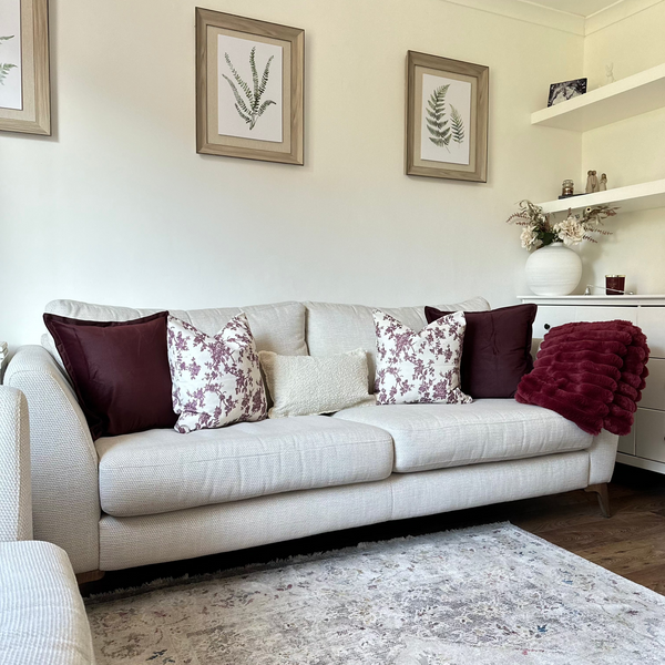 As set of 5 cushions sat on a cream sofa, displaying the velvet plum cushion combine with similar coloured cushions to create a cohesive look