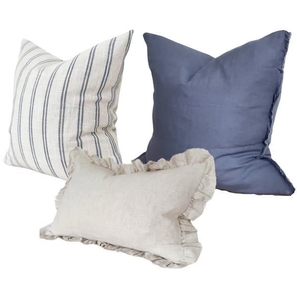 1 square off white cotton cushion with a repeating double vertical stripe left to right. 2 square weathered edge linen navy blue cushions and 1 rectangle cream linen ruffled edge cushion. sat on a plain white background