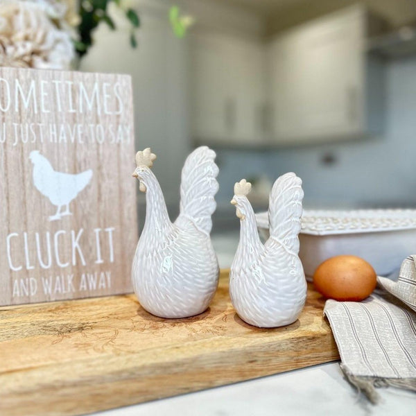 2 Neutral Chicken Ornaments one small and one large, Both sat on a wooden chopping board in a country style kitchen