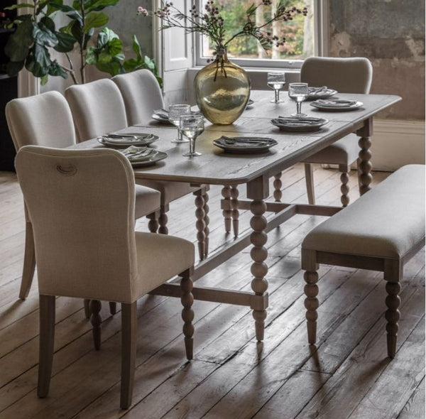 extending wooden rectangle dining table with an oak colour and beautiful wood grain and bobbin style legs. Sat in a country style home with matching oak bobbin fabric dining chairs surrounding it 