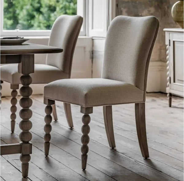 Cream linen fabric dining chair. Front legs are wooden oak coloured round bobble effect. Back legs straight wooden oak effect for stability. Sat in a country style dining room