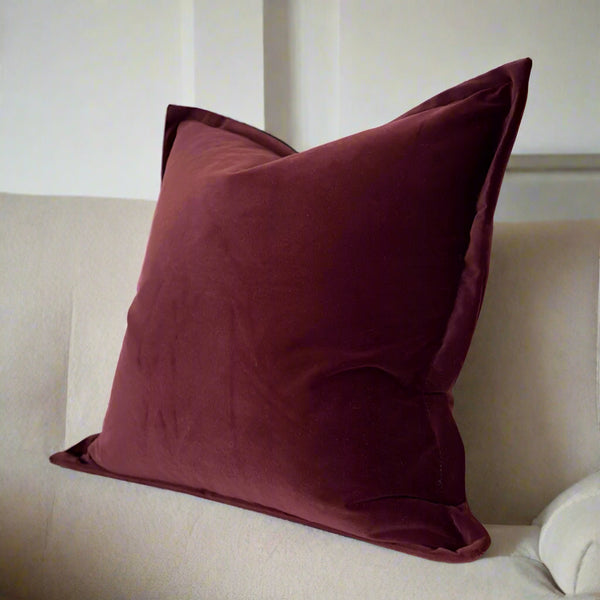 Square plum/burgundy velvet feel cushion sat on a cream sofa