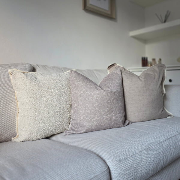 Set of 3 cushions. one square greige with a cream piped scalloped edge, one square greige cushion with an all over greige leaf print, 1 square cream boucle cushion all sat on a cream sofa