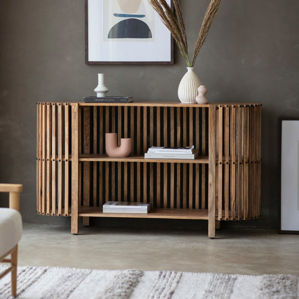 Vindr Mango Wooden Slatted Sideboard with vertical wooden slats on each side and an open shelf front to display vases, books etc. sat in a moody living room