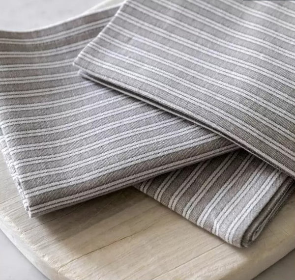 Close up of the cream and grey striped cotton napkins. Folded on a light, wooden chopping board on a kitchen counter for styling.