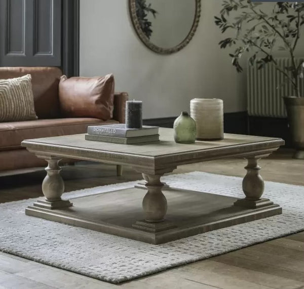 Chunky wooden coffee table with  a square top and square bottom, column like corners attaching the square wooden top to the wooden bottom. In a living room setting