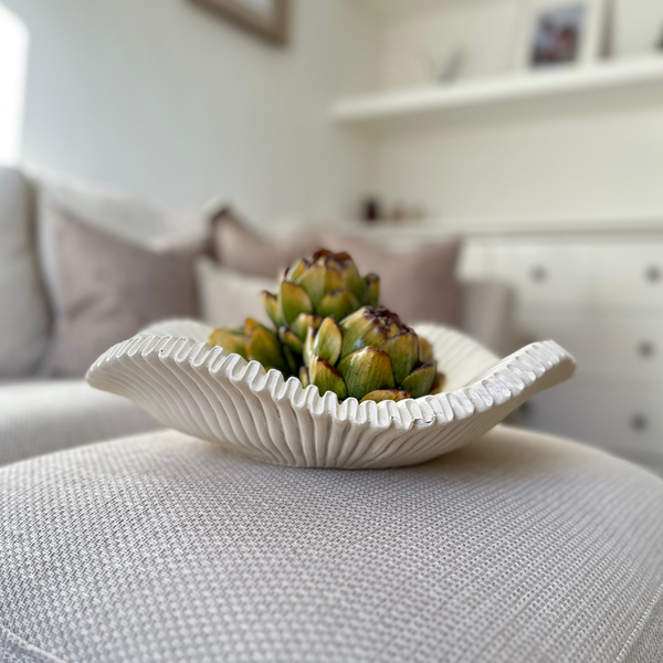 White scalloped edge decorative large bowl, with decorative green artichokes inside. Sat in the centre of a white sideboard