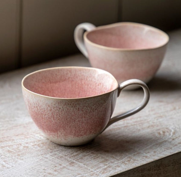 Pink cute set of 2 mugs with an imperfect round shape and a cute handle.  2 tone pink and cream more pink on top blending to a soft cream on the bottom. Both sat on a wooden worktop