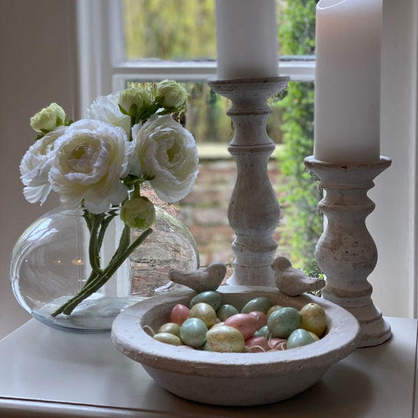 Stone bird bath with 2 stone birds sat around the edge of the bowl. Sat on a sideboard filled with decorative pastel easter eggs for decoration